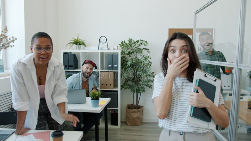 Trabalhadores emocionais do escritório apontando para a câmera e rindo fazendo rostos engraçados dentro do local de trabalho