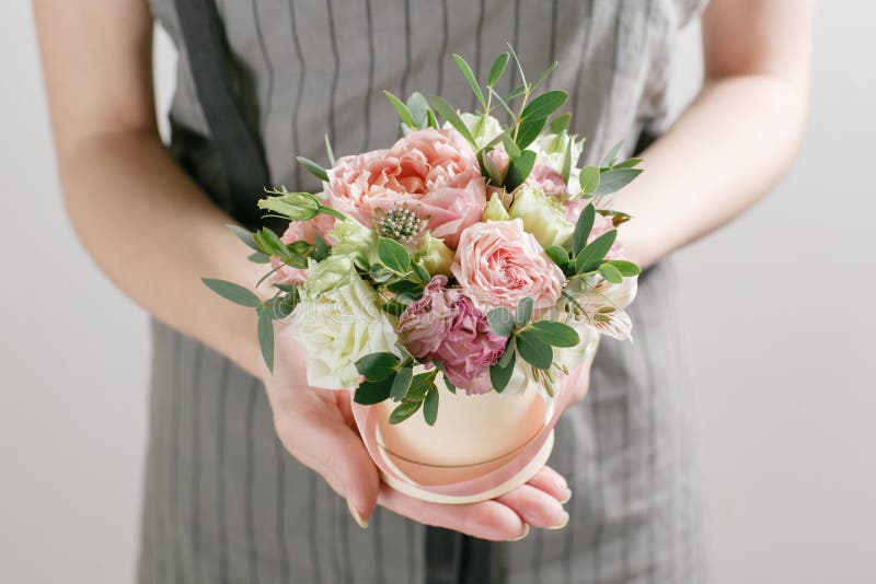 Work florist, bouquet in a round box. smelling flowers holding peach roses bouquet in hat box against the plastered wall. Work florist, bouquet in a round box. smelling flowers holding peach roses bouquet in hat box against the plastered wall.