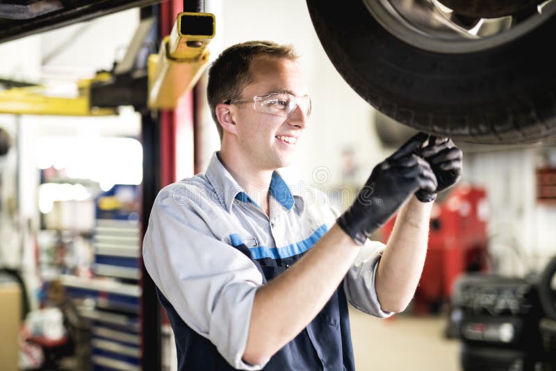 Trabalho considerável do mecânico no uniforme que trabalha no desgaste do pneu da verificação do carro fotografia de stock Trabalho considerável do mecânico no uniforme que trabalha no desgaste do pneu da verificação do carro fotografia de stock