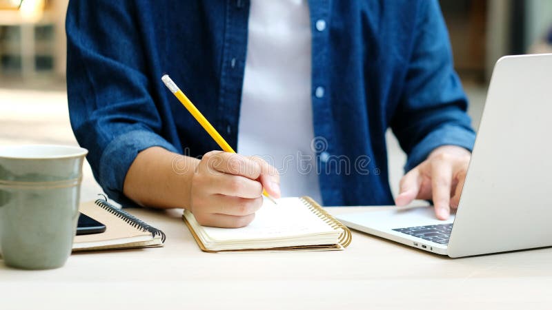 Trabalho de educação online a partir de casa, escrevendo à mão sobre o notebook e usando o computador portátil, estudante adulto d