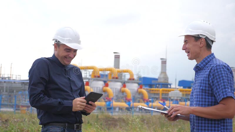 Trabalho em equipe conceito de estação de produção de gás industrial vídeo em câmera lenta dois engenheiros em capacetes balançan