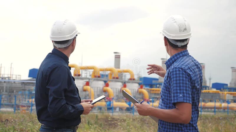 Trabalho em equipe. conceito de estaÃ§Ã£o de produÃ§Ã£o de gÃ¡s industrial. vÃ­deo em cÃ¢mera lenta. dois engenheiros em capacete