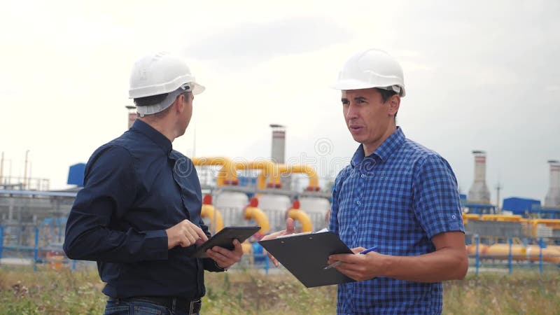 Trabalho em equipe conceito de estação de produção de gás industrial Vídeo de movimento lento Dois engenheiros em capacetes estud