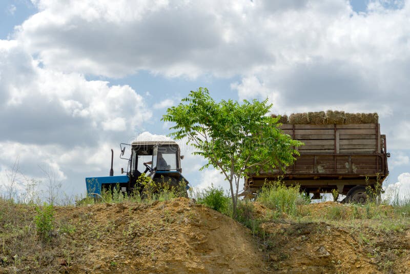 Tractor azul con el heno en paseos de un remolque al borde de un acantilado fotografía de archivo libre de regalías Tractor azul con el heno en paseos de un remolque al borde de un acantilado fotografía de archivo libre de regalías