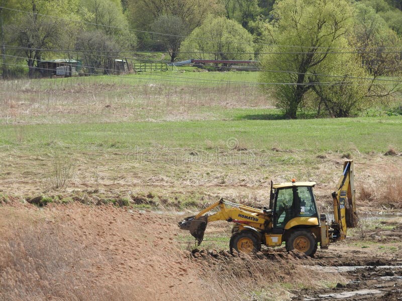 Tractor on the Construction Site Against the River, Trees and Sky Stock