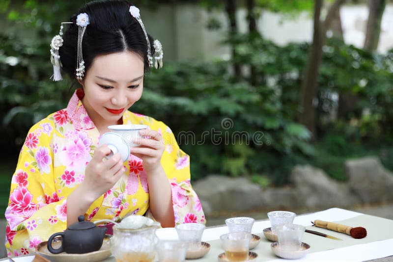 Traditional Asian Japanese beautiful Geisha woman wears kimono show tea art ceremony drink tea in a summer spring outdorr garden