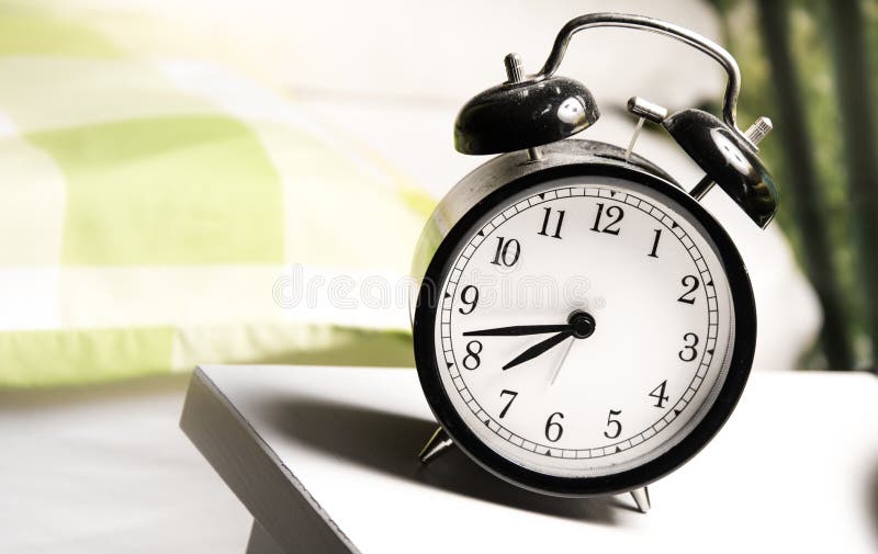 Traditional black and white alarm clock standing on a white table next to a green and white bed duvet