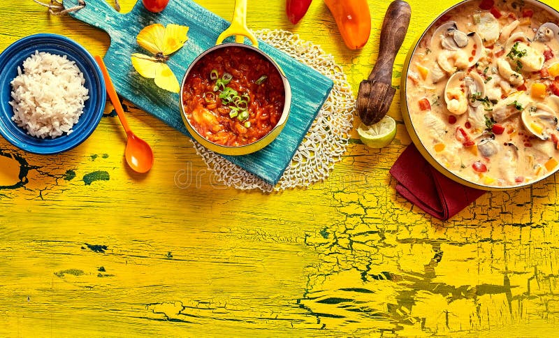 Traditional Brazilian shell casserole with Venus shells in a creamy spicy sauce served with side dishes of rice and chili dip ona colorful tropical yellow picnic table with copy space, top view. Bivalve shell stock images, royalty-free photos and pictures