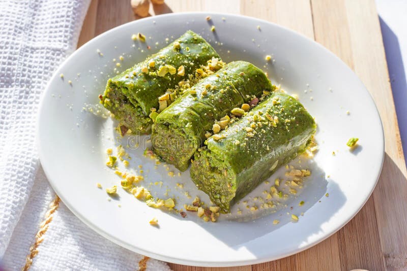 Traditional East Asian sweet baked pistachio baklava or pahlava with nuts and syrup on a white plate stock image Traditional East Asian sweet baked pistachio baklava or pahlava with nuts and syrup on a white plate stock image