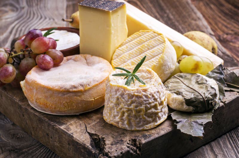Traditional French cheese platter with soft and hard cheese and fruits on a rustic wooden board