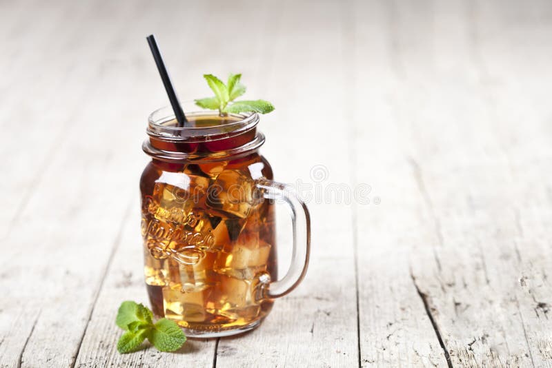 Traditional iced tea with lemon, mint leaves and ice cubes in glass jar on rustic wooden table background