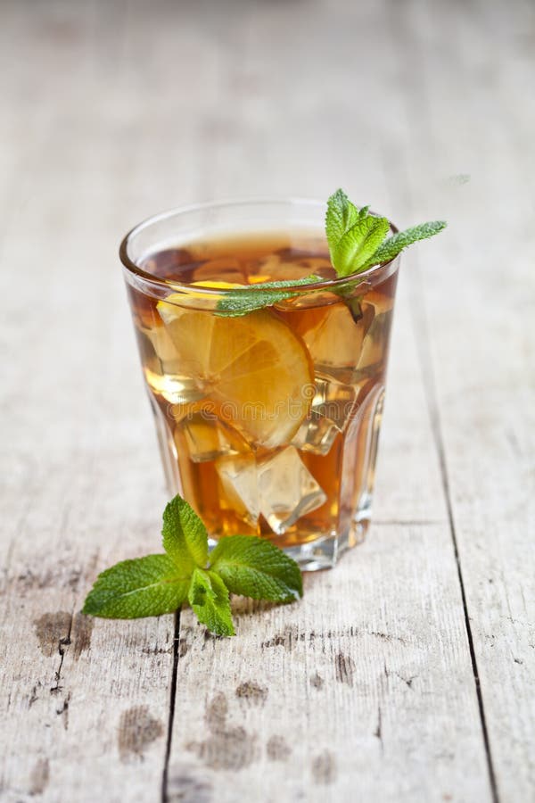 Traditional iced tea with lemon, mint leaves and ice in glass on rustic wooden table