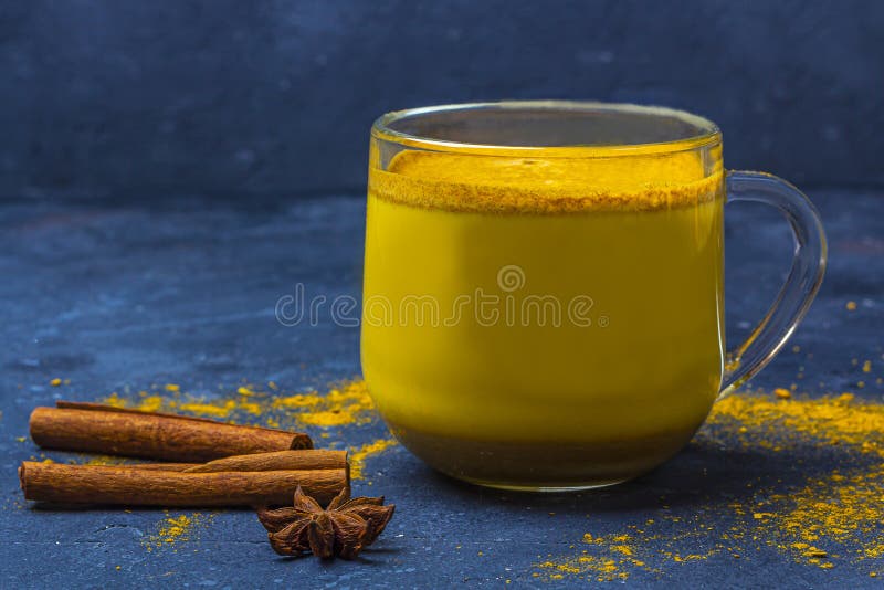 Traditional Indian drink turmeric milk is golden milk in glass mug with cinnamon, anis star, turmeric on dark background. Weight