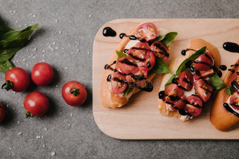 traditional italian bruschetta on wooden board, basil and fresh tomatoes on grey stock photos traditional italian bruschetta on wooden board, basil and fresh tomatoes on grey stock photos