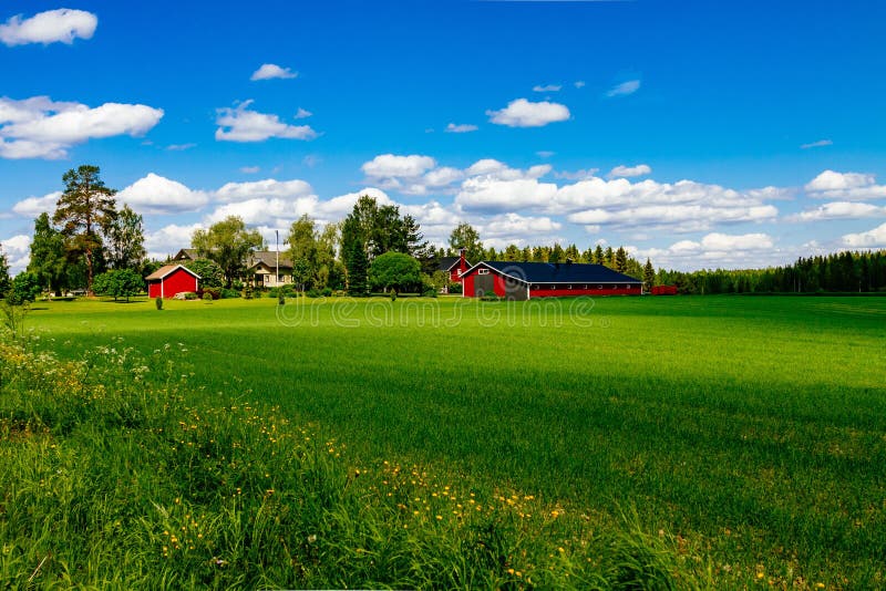 Traditional red farm house barn with white trim in open pasture with blue sky in Finland