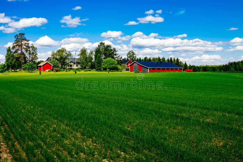 Traditional red farm house barn with white trim in open pasture with blue sky in Finland