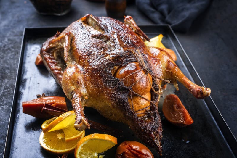 Traditional roasted stuffed Christmas duck with quinces and orange slices on a rustic metal tray on a black board