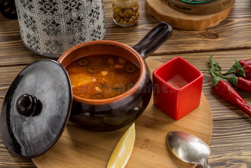 Traditional Russian soup solyanka with smoked meat and olives in clay pot on wooden table stock images Traditional Russian soup solyanka with smoked meat and olives in clay pot on wooden table stock images