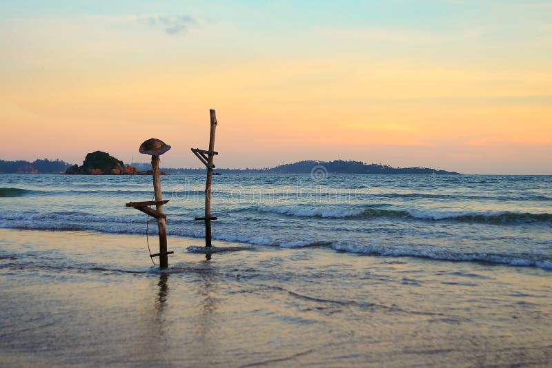 Traditional Sri Lankan poles for fishing. One of them has a hat. Beach of the ocean at sunset. royalty free stock photos Traditional Sri Lankan poles for fishing. One of them has a hat. Beach of the ocean at sunset. royalty free stock photos