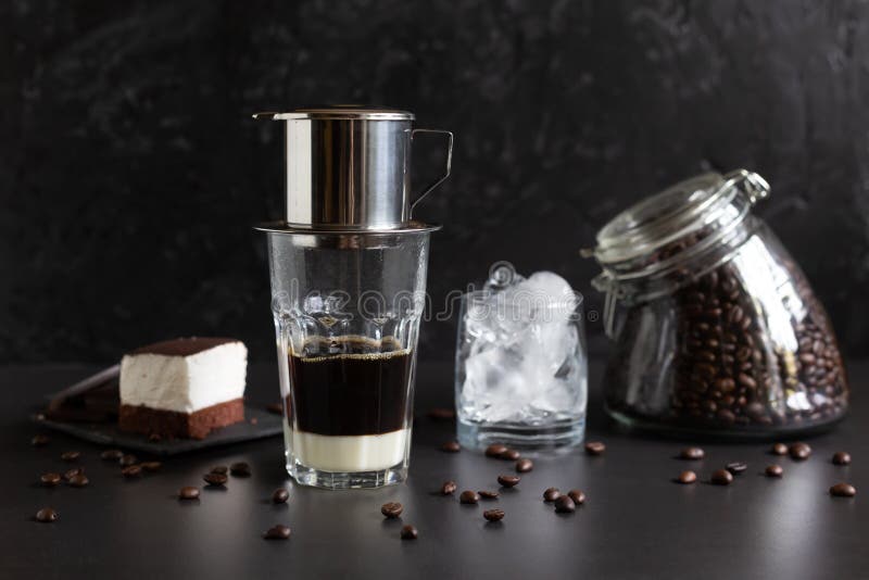 Traditional vietnamese coffee maker placed on the top of glass, glass jar with coffee beans, glass with ice and souffle dessert