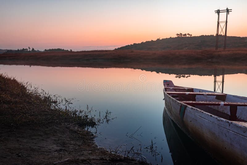 Traditional wood boat at calm lake with dramatic sunrise colorful sky reflection at morning in details.