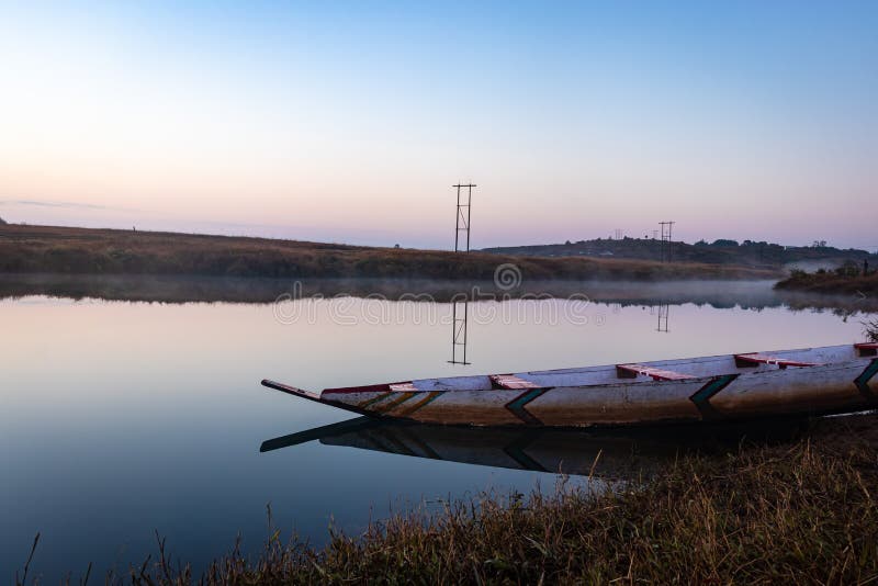 Traditional wood boat at calm lake with dramatic sunrise colorful sky reflection at morning in details.