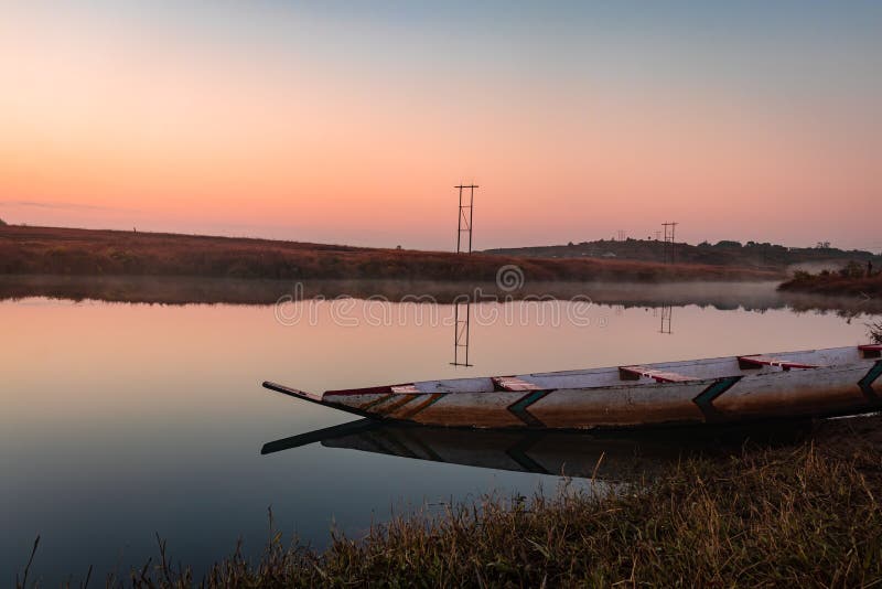 Traditional wood boat at calm lake with dramatic sunrise colorful sky reflection at morning in details.