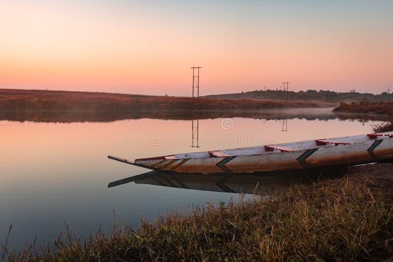 Traditional wood boat at calm lake with dramatic sunrise colorful sky reflection at morning in details.