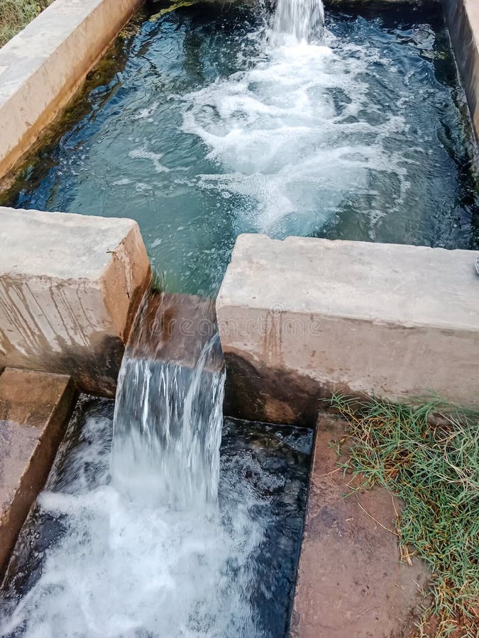 Traditionell vattenkälla från rörbrunn på landsbygden. vattenflödet fritt från en betongstruktur till en liten pool arkivfoton