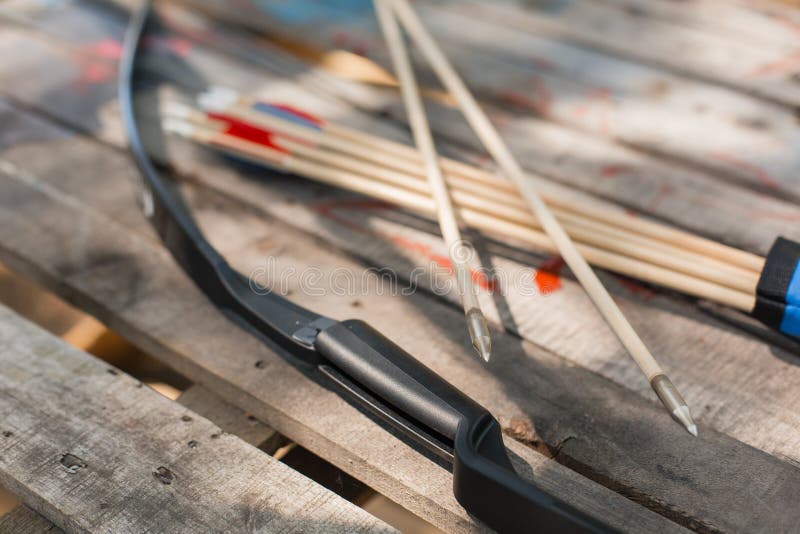 Traditional wooden arrows with feather fletching and a wooden bow in the background. Wooden archery homemade arrows with plastic nocks and natural feathers. Bow and Arrows. Traditional wooden arrows with feather fletching and a wooden bow in the background. Wooden archery homemade arrows with plastic nocks and natural feathers. Bow and Arrows