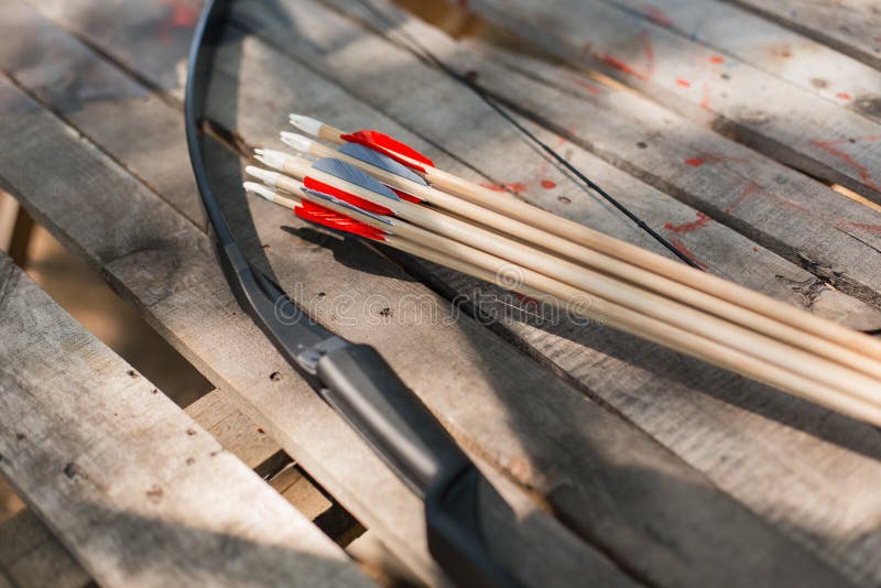 Traditional wooden arrows with feather fletching and a wooden bow in the background. Wooden archery homemade arrows with plastic nocks and natural feathers. Bow and Arrows. Traditional wooden arrows with feather fletching and a wooden bow in the background. Wooden archery homemade arrows with plastic nocks and natural feathers. Bow and Arrows