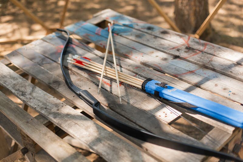 Traditional wooden arrows with feather fletching and a wooden bow in the background. Wooden archery homemade arrows with plastic nocks and natural feathers. Bow and Arrows. Traditional wooden arrows with feather fletching and a wooden bow in the background. Wooden archery homemade arrows with plastic nocks and natural feathers. Bow and Arrows