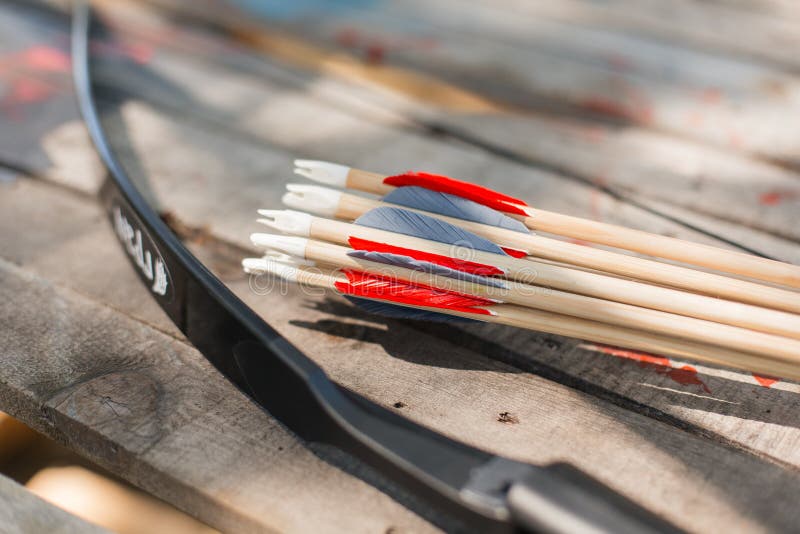 Traditional wooden arrows with feather fletching and a wooden bow in the background. Wooden archery homemade arrows with plastic nocks and natural feathers. Bow and Arrows. Traditional wooden arrows with feather fletching and a wooden bow in the background. Wooden archery homemade arrows with plastic nocks and natural feathers. Bow and Arrows