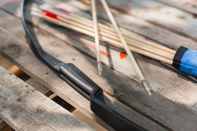 Traditional wooden arrows with feather fletching and a wooden bow in the background. Wooden archery homemade arrows with plastic nocks and natural feathers. Bow and Arrows. Traditional wooden arrows with feather fletching and a wooden bow in the background. Wooden archery homemade arrows with plastic nocks and natural feathers. Bow and Arrows