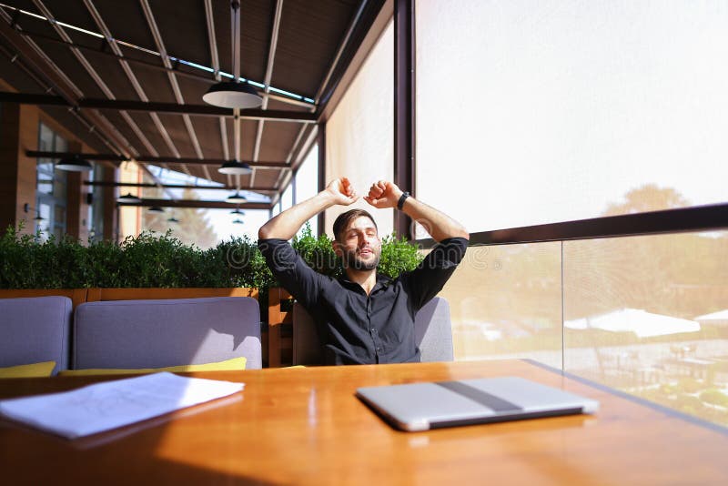 European translator sorting papers and closing laptop lid at cafe. Young persistent man dressed in black shirt looks happy and successful. Concept of finishing work and resting. European translator sorting papers and closing laptop lid at cafe. Young persistent man dressed in black shirt looks happy and successful. Concept of finishing work and resting.