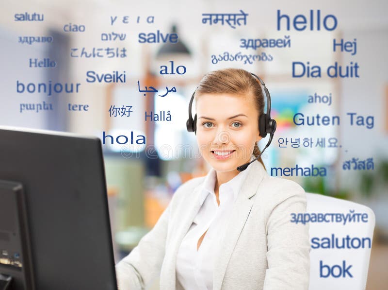 Translation, business and technology concept - smiling female translator or operator with computer at office over greeting words in different foreign languages. Translation, business and technology concept - smiling female translator or operator with computer at office over greeting words in different foreign languages