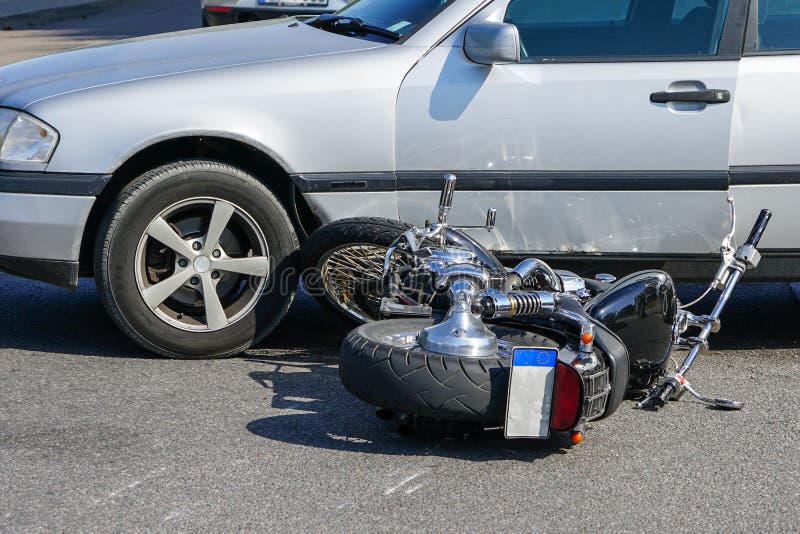 Traffic accident, motorcycle collision with a car on city street, overturned motorcycle