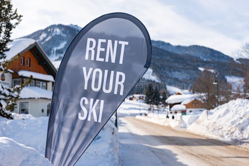 Rent your ski advertising flag. Winter services at ski region Schladming Dachstein, Austria. Snow covered road, house and mountain