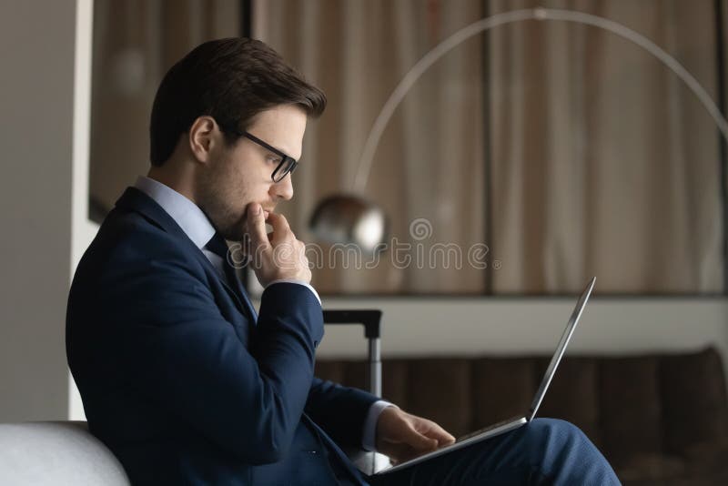 Tragen Brille des aufwändigen Geschäftsmannes der Datenzugriffsseiten-Ansicht, die Kinn mithilfe des Notebooks berührt. lizenzfreies stockfoto