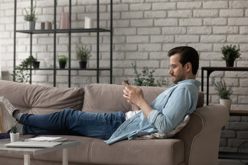 Tragen Brille des Seitenansichtmannes mithilfe des Telefons, das auf der Couch liegt lizenzfreies stockfoto