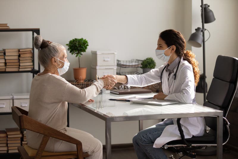 Tragen Gesichtsmaske Seitenansichtdoktors und reifer geduldiger Handschlag lizenzfreies stockbild