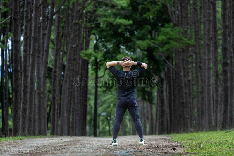 Alergătorul în camuflajul negru se întinde pentru a se încălzi în aer liber pe șoseaua pădurii de pin pentru activități de exerciț stock photography