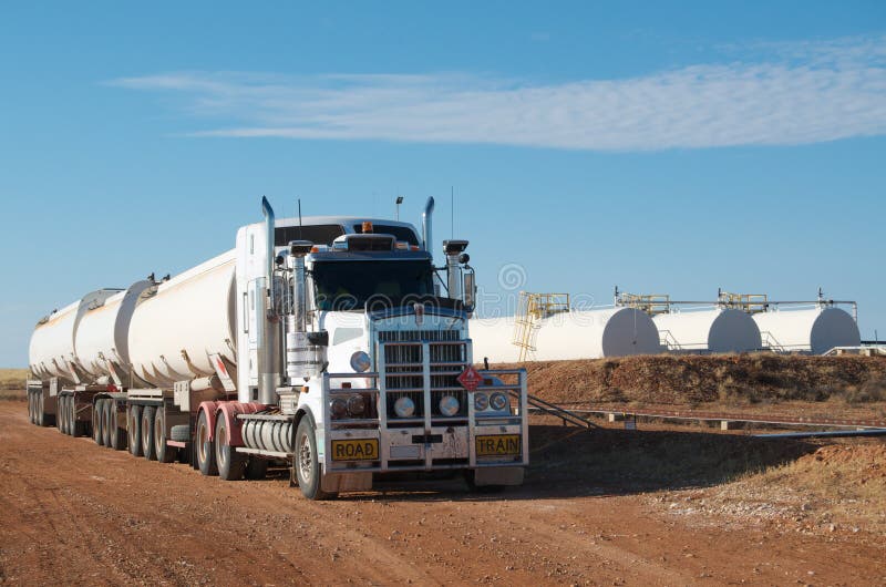 Australian triple road train filling up with crude oil at oilfield, outback Australia; three white storage tanks in background. Australian triple road train filling up with crude oil at oilfield, outback Australia; three white storage tanks in background