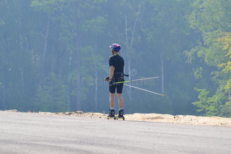 Training an athlete on the roller skaters. Biathlon ride on the roller skis with ski poles, in the helmet. Autumn workout. Roller stock photography Training an athlete on the roller skaters. Biathlon ride on the roller skis with ski poles, in the helmet. Autumn workout. Roller stock photography