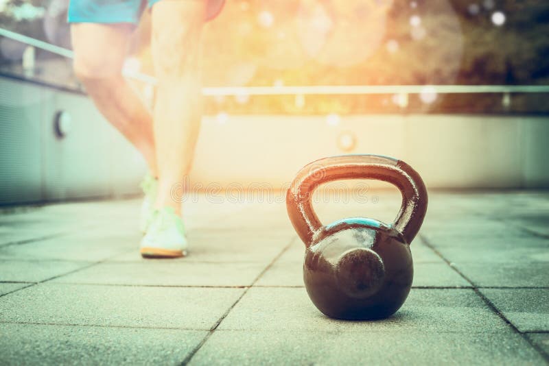 Training process with the kettlebell in the fresh air, young man trains nature background