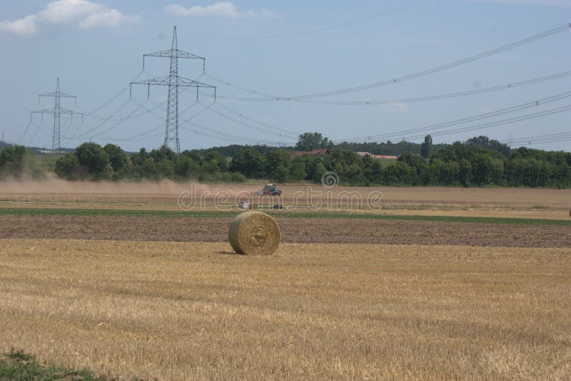 Traktor im Abstand, ein Feld nach der Sommerernte eggend und oben werfen Staubwolken, mit Strohballen im Vorderteil stockbild Traktor im Abstand, ein Feld nach der Sommerernte eggend und oben werfen Staubwolken, mit Strohballen im Vorderteil stockbild