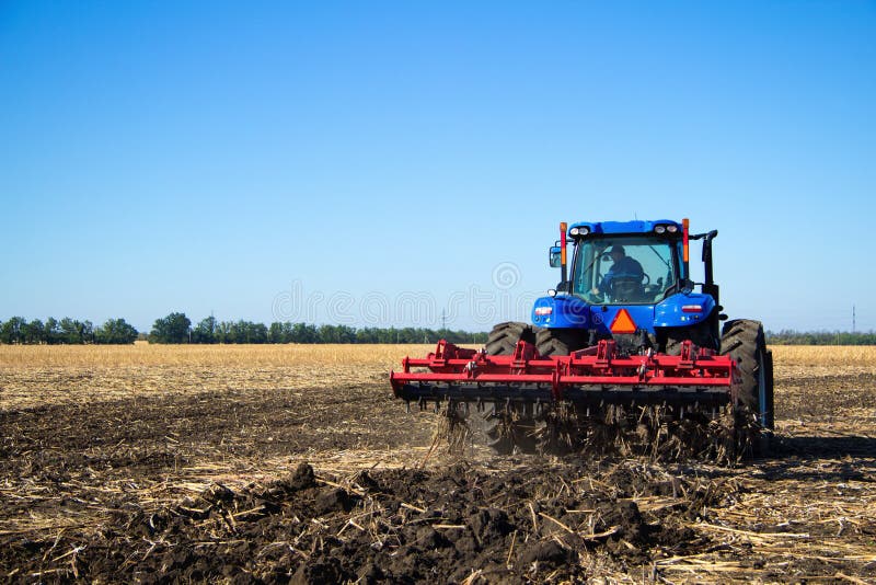 Tractor with plow working on the farm, a modern agricultural transport, a farmer working in the field, preparing the land for planting, tractor on the background of blue sky, working plowed field. Tractor with plow working on the farm, a modern agricultural transport, a farmer working in the field, preparing the land for planting, tractor on the background of blue sky, working plowed field