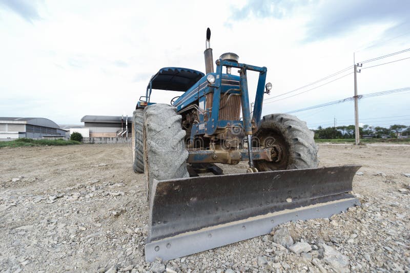 Traktorblått parkerat i en färdigbyggd avskiljning. Traktorblått parkerat i en avskiljning för att förbereda för matjord och en vacker blå himmel i bakgrunden. Begreppet bulldozer bereder toppmarken för byggnation.