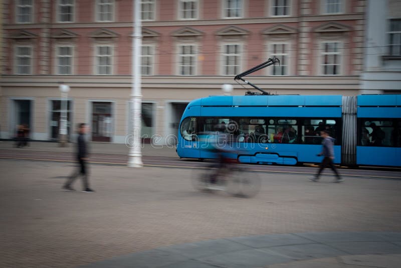Tram blu che passa per la strada della città con pedoni e ciclisti sfuocati fotografia stock