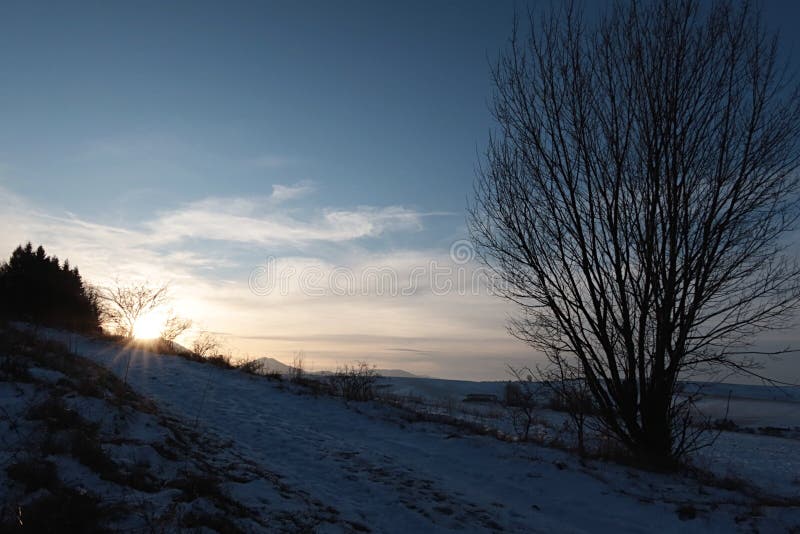 Tramonto sulla strada della neve invernale e sulle campagne con campi agricoli sotto le montagne basse di Tatras fotografie stock Tramonto sulla strada della neve invernale e sulle campagne con campi agricoli sotto le montagne basse di Tatras fotografie stock